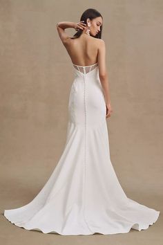 a woman in a white wedding dress is looking down at the back of her gown