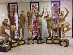 a group of young women standing next to each other in front of a wall with trophies