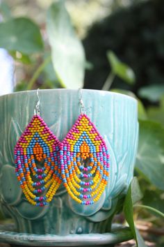 These stunning Native American beaded earrings are handcrafted with intricate geometric designs, featuring vibrant Pink, Blue, Orange, and Yellow. Each pair is made with care and respect for traditional beadwork techniques, creating bold statement pieces perfect for any occasion. Add a touch of authentic cultural artistry to your style with these lightweight and eye-catching earrings. Colors may appear slightly different in person due to variations in computer monitors. Native American Beaded Earrings, Bead Weaving Patterns, Boho Geometric, Black Seed, Native American Beading, Geometric Jewelry, Weaving Patterns, Earrings Blue, Bead Jewelry