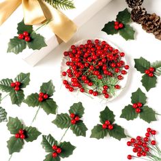 holly and red berries on a white plate next to pine cones, evergreen leaves and ribbon