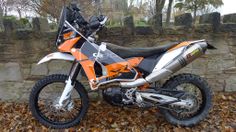 an orange and black dirt bike parked next to a stone wall