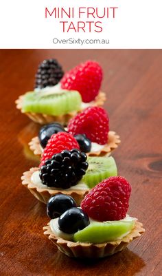 mini fruit tarts are lined up on a table with berries and kiwis