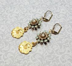 Pretty 10k gold plated maiden charms dangle beneath embellished vintage brass connectors. The connectors are set with glass rhinestones in chrysolite opal color (light seafoam green) and clear crystal with a glass pearl center. These earrings are 2-1/4 inches long including the leverback earwires. Make a glamorous statement with this elegant pair of earrings✨ ✨ Note: I do my best to take accurate photos. Please be aware that colors and brightness can vary slightly between different monitors and Nickel-free Vintage Gold-plated Earrings, Vintage Gold Plated Nickel Free Earrings, Victorian Dangle Earrings With Vintage Charm, Jeweled Antique Gold Brass Jewelry, Brass Jeweled Drop Earrings, Victorian Brass Earrings With Vintage Charm, Antique Gold Jeweled Earrings, Gold Dangle Earrings Costume Jewelry, Bohemian Jeweled Gold Earrings