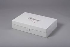 a white box with the lid open on a gray surface, showing the logo and side opening