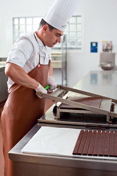 a man wearing an apron and hat preparing food in a kitchen with a conveyor belt