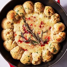 a skillet filled with bread and cheese covered in rosemary garnish on top of a white table