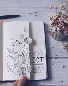 a hand holding an open notebook with flowers on it and the number 10 october written in black ink