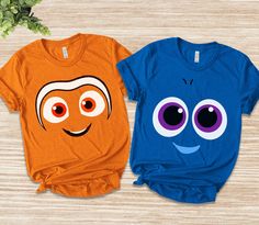 two t - shirts with faces on them are sitting next to each other, one is orange and the other is blue