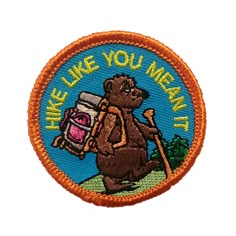 a patch with a bear holding a backpack and the words, like like you mean it