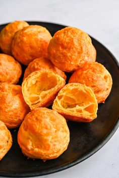 a black plate filled with orange pastries on top of a white tablecloth covered floor