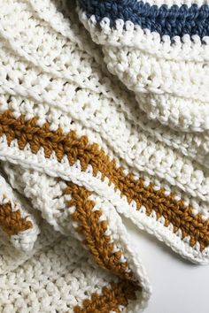 a crocheted blanket is laying on top of a white surface with brown and blue stripes