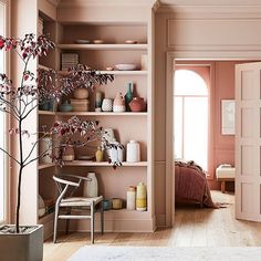 a living room with pink walls and shelves filled with vases, plants and other decorative items