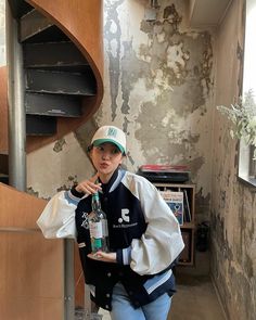 a woman is holding a bottle in her hand and standing next to a spiral staircase