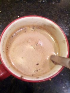 a cup of coffee with a spoon in it on a counter top next to a knife