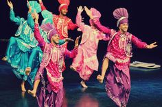 some people are dancing on stage with their arms in the air and one person is wearing a turban