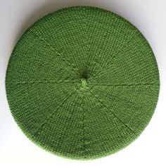 a green knitted round cushion on a white surface with the center section showing an intricate design