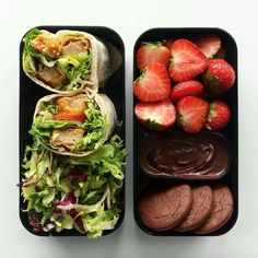 two black trays filled with different types of food and some strawberries on the side