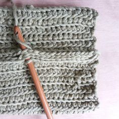 a crocheted dishcloth with a wooden handle on a pink surface, next to a knitting needle