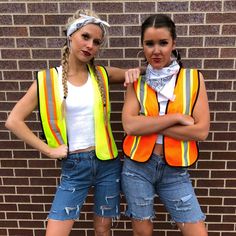 two young women standing next to each other in front of a brick wall wearing safety vests