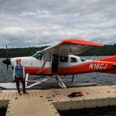 a woman standing on a dock next to an airplane that is parked at the water's edge