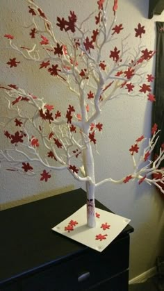 a white tree with red leaves on it in front of a black dresser and wall