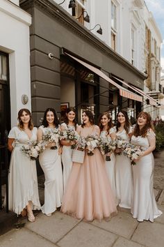 a group of women standing next to each other in front of a building holding bouquets