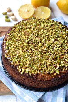 a chocolate cake with pistachio toppings on a wooden cutting board next to sliced lemons