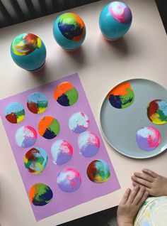 a child's hand is next to some painted eggs on a table with paper