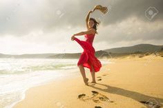 a woman in a red dress is dancing on the beach