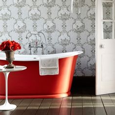 a red bath tub sitting on top of a wooden floor next to a white door