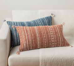 two pillows sitting on top of a white couch next to a pillow with tassels