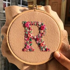 a person holding up a cross stitched letter with flowers on the front and bottom