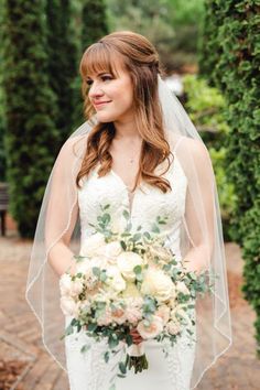 a woman in a wedding dress holding a bridal bouquet and smiling at the camera