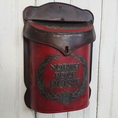 a red mailbox mounted to the side of a white wooden wall with words north pole post on it