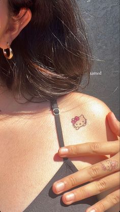 a woman with a hello kitty tattoo on her chest and hand next to her ear