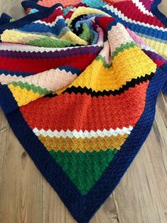 multicolored crocheted blanket laying on wooden floor next to folded up scarf