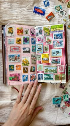 a person is holding an open book with stamps on it and there are many other items scattered around