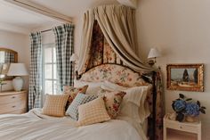 a bed with lots of pillows on top of it next to a dresser and window