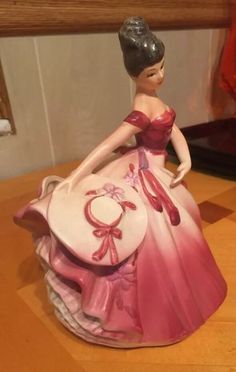 a figurine is sitting on a table with a dress and hat in front of it