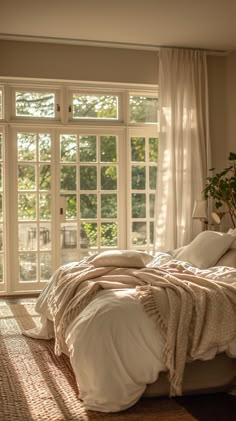 a bed sitting in a bedroom next to a window covered in white sheets and blankets