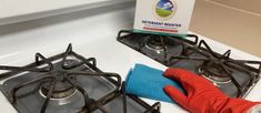 a person in red gloves is cleaning the stove top with a blue cloth and rag