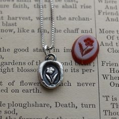 a close up of a necklace on top of an open book with a red stone