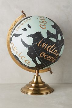 a globe with words written on it sitting on top of a metal stand in front of a white wall