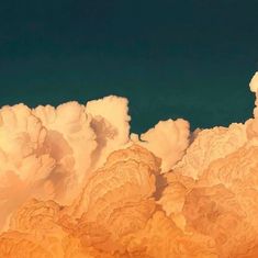 the sky is filled with fluffy clouds and blue water in the distance, as well as an airplane flying overhead