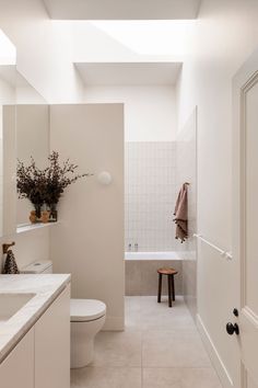 a white bathroom with a toilet, sink and bathtub next to a mirror on the wall