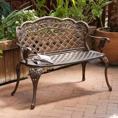 a metal bench sitting on top of a brick floor next to potted planters