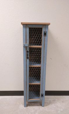 an old blue cabinet with chicken wire on the top and bottom shelves, against a white wall