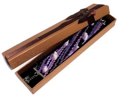 an open box with a purple and black beaded bracelet in it