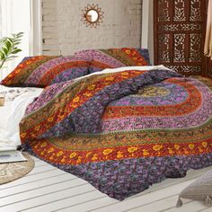 a bed covered in a colorful comforter next to a white brick wall with a potted plant