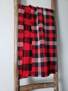 a red and black checkered blanket sitting on top of a wooden chair next to a white wall